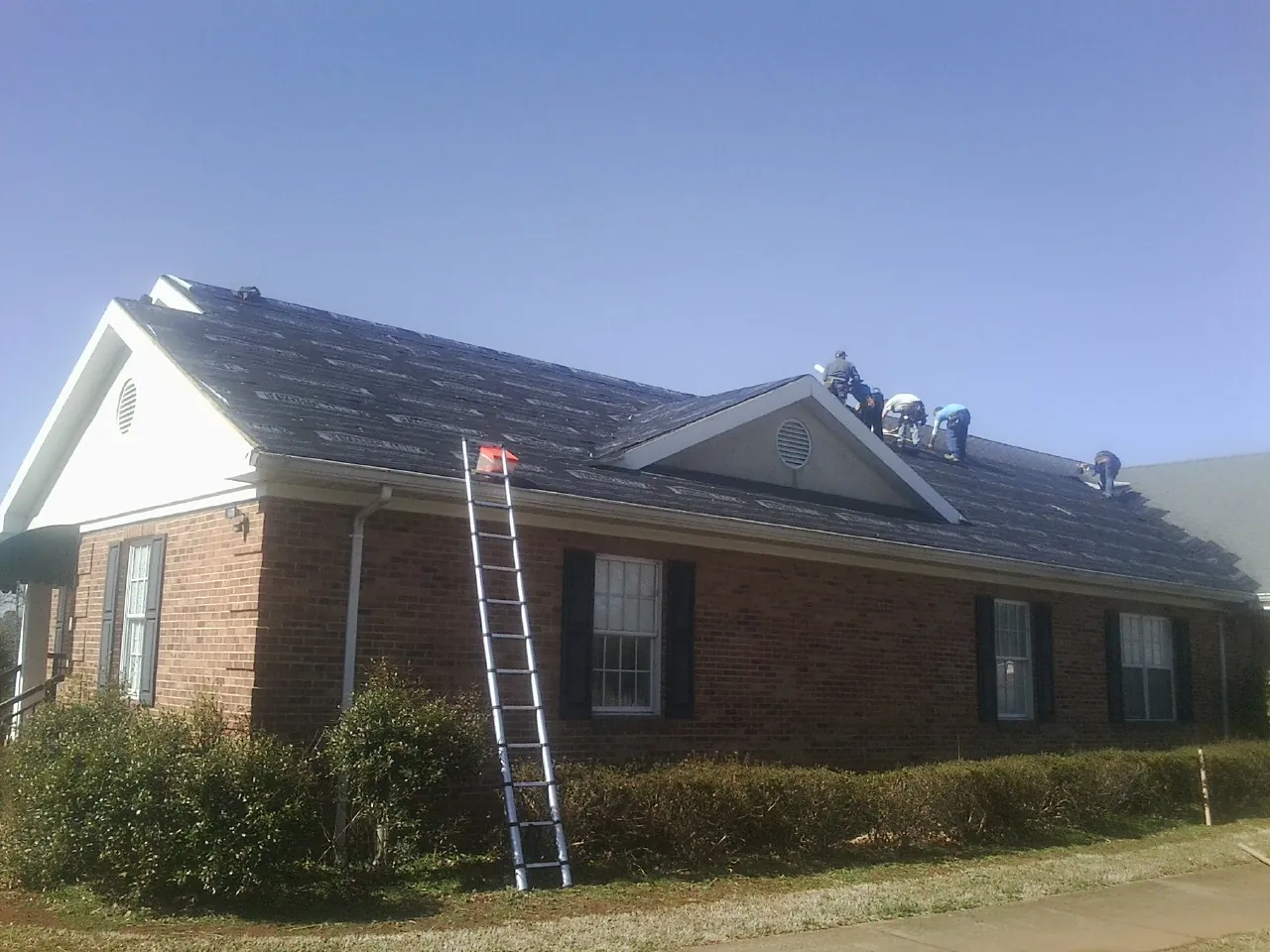 Crew tearing shingles off a brick ranch roof with a ladder set — Emergency Roof Repair work by our crew in Endicott