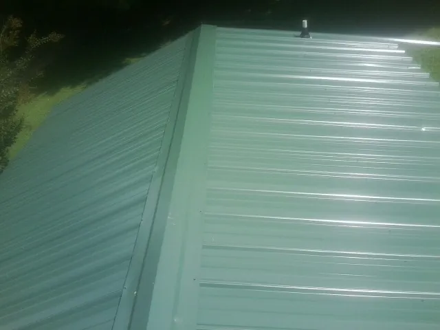 New green metal panels meeting at the ridge of a roof — Flat Roof Repair work by our crew in Endicott