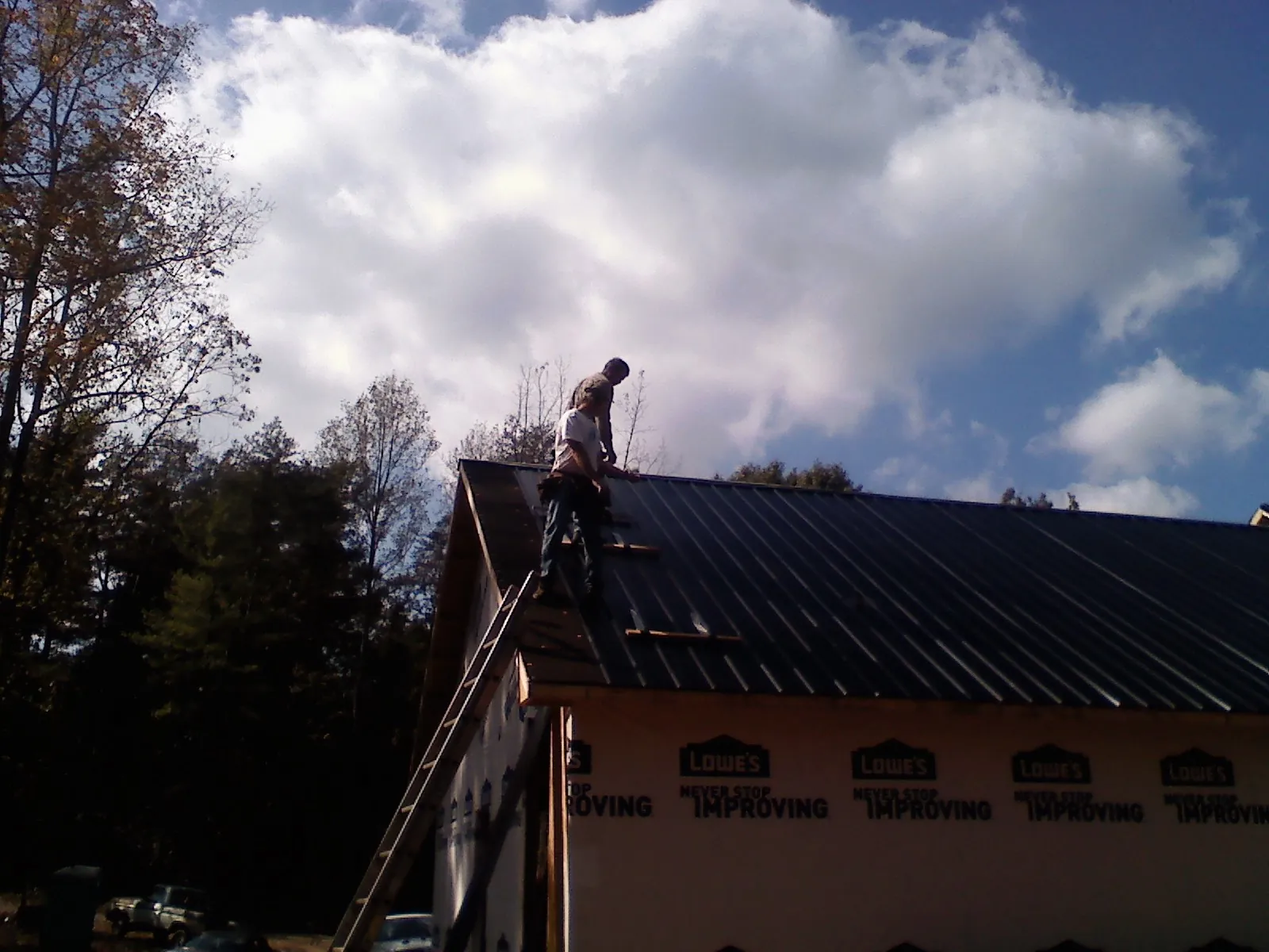 Roofer fastening dark metal panels high against a cloudy sky, from a Roof Inspection job in Endicott